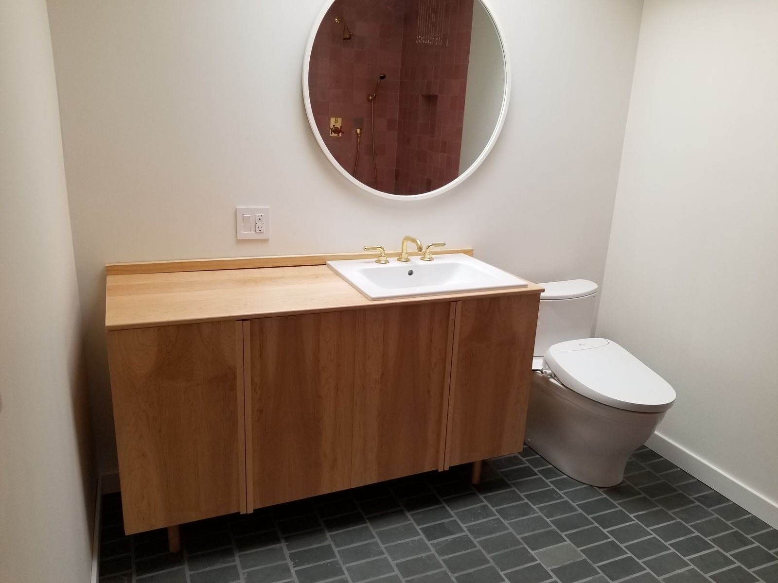Bathroom with a wood vanity, round mirror and green floor tile
