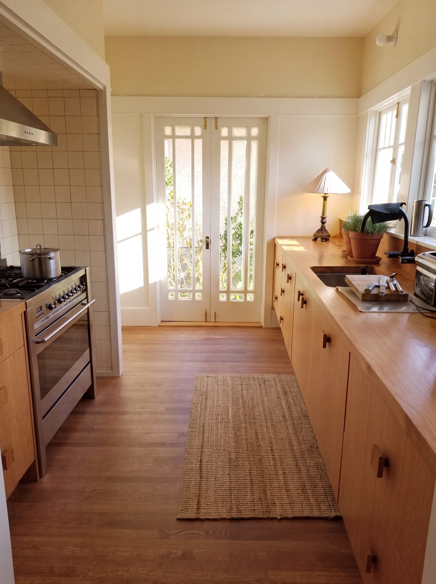 Sunlit Craftsman galley kitchen with wood cabinets, a solid wood counter and restored French doors