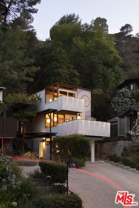 Three-story hillside home at dusk surrounded by trees
