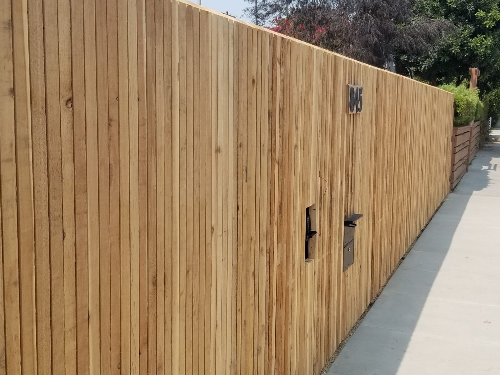 Tall vertical wood privacy fence along a sidewalk